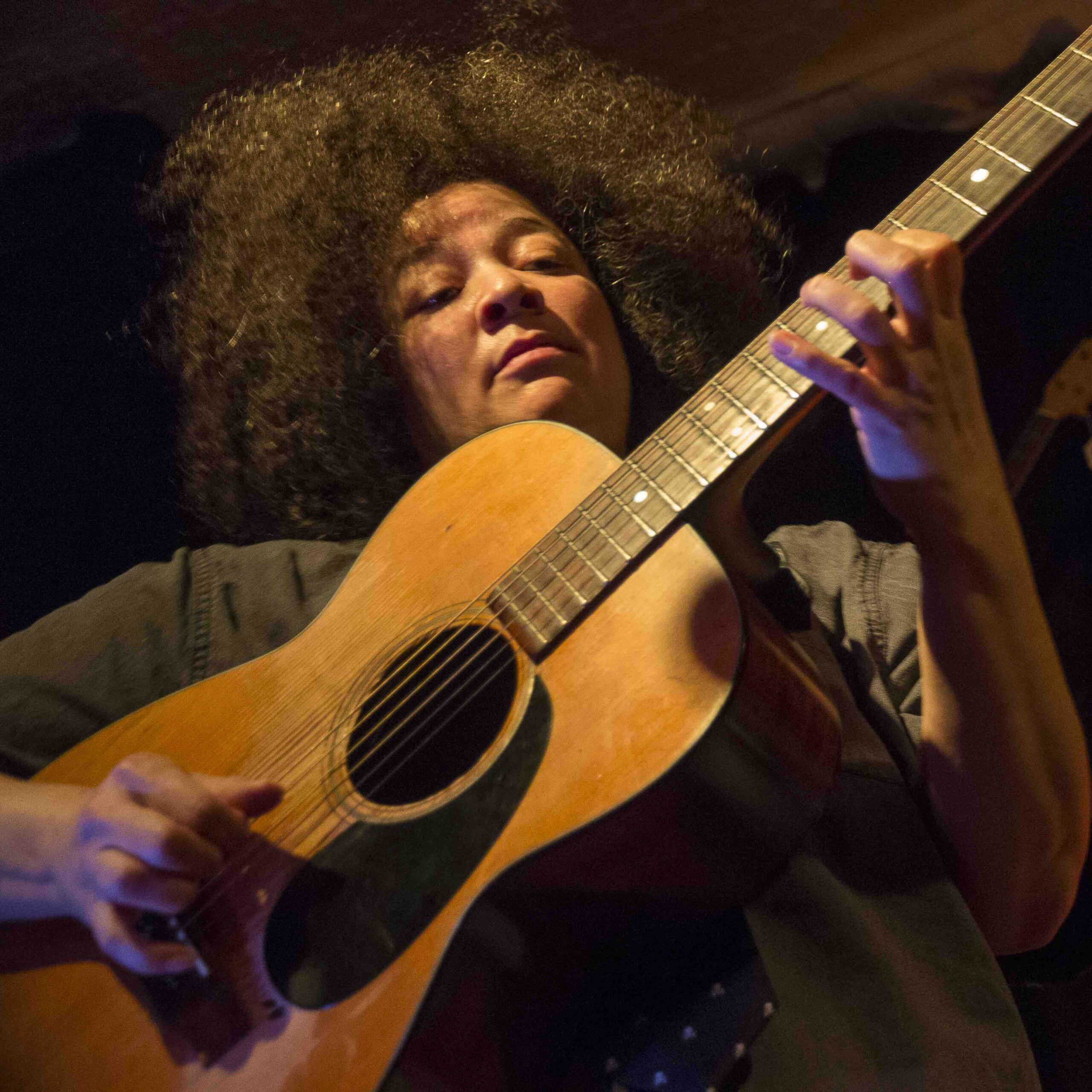 Pamela Means playing an acoustic guitar.